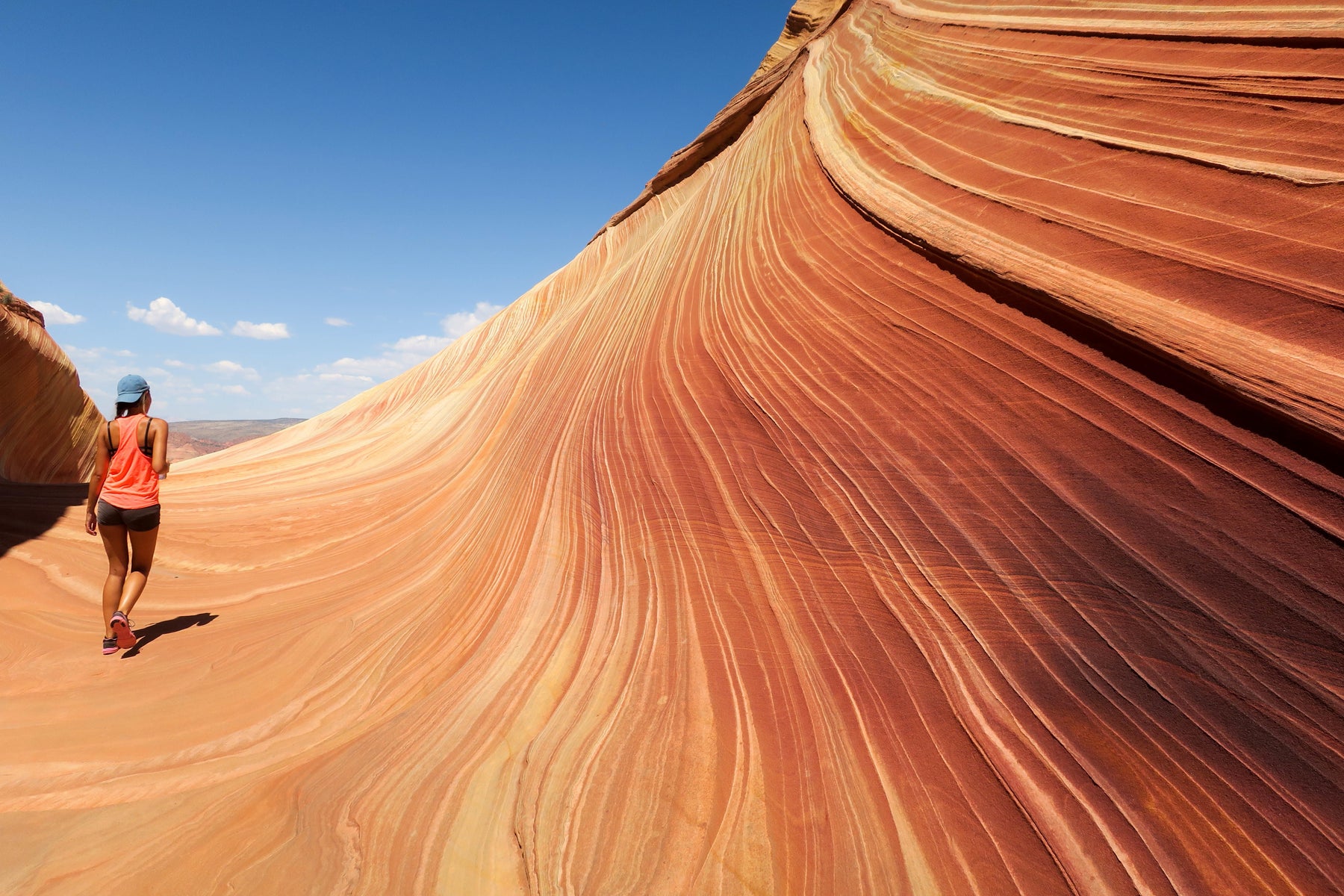 Woman hikes at The Wave, orange-striated rock formation at Vermilion Cliffs.